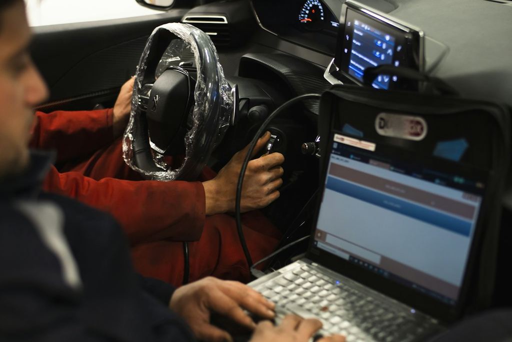 A technician running a scan tool from a laptop inside a car